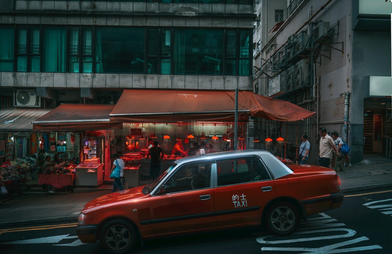 A red taxi drives past a food stall.